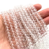 A hand holds a strand of clear pink Austrian faceted crystal beads for jewelry making.