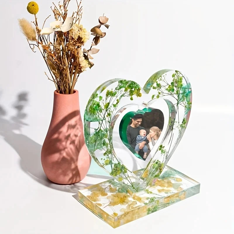 A heart-shaped clear silicone mold filled with green foliage and a framed photo of a baby.