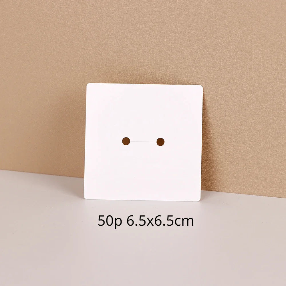 A white square jewelry display card with two small holes is shown on a light surface.