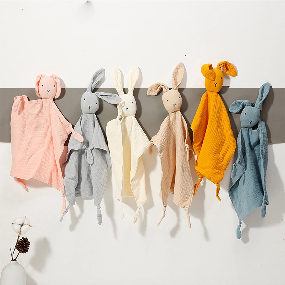 A collection of soft cotton muslin baby comforters shaped like rabbits in various pastel and warm tones.