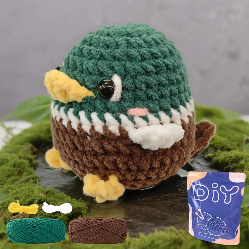 A finished green and brown crochet amigurumi bird with yellow accents, next to yarn supplies.