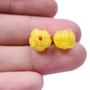 Two small yellow glass charm pendants shaped like flowers are held between fingers.