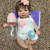 A realistic soft silicone reborn doll with pink hair, floral accessories, and a purple book lying next to it.