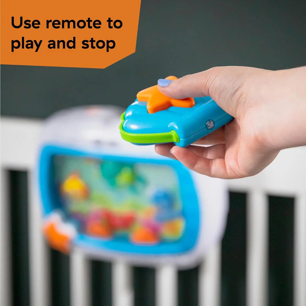 A hand uses a remote to play and stop an ocean-themed crib soother with lights and melodies.
