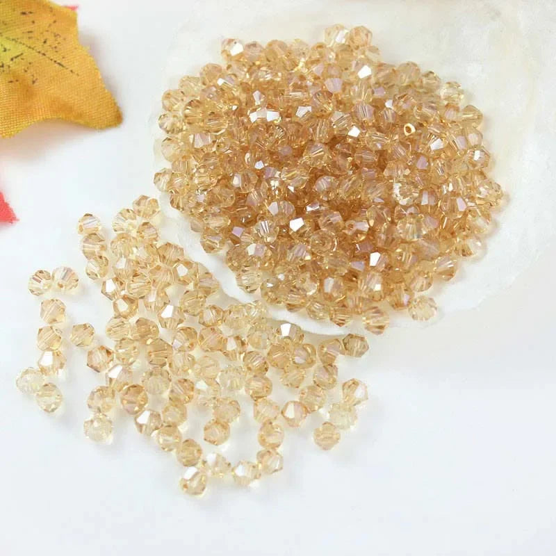 A pile of small, faceted, golden-amber crystal beads for jewelry making is shown on a white surface.