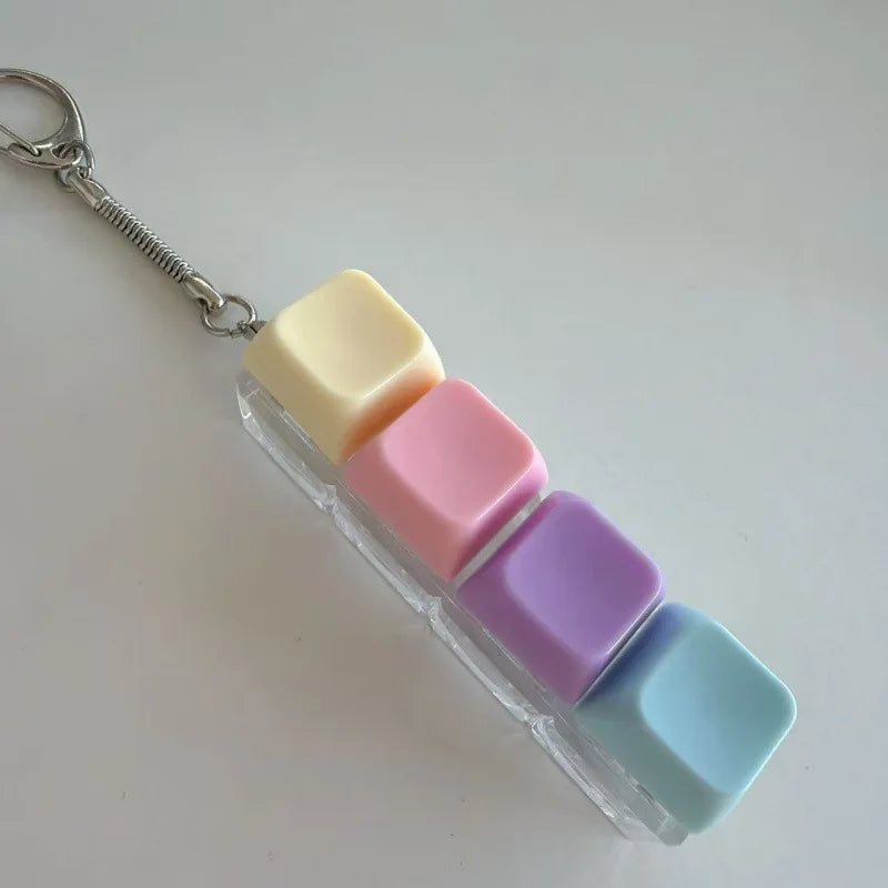 A pastel keyboard keychain fidget toy featuring square silicone pieces in yellow, cream, pink, and purple.