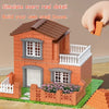 A small brick house model built from orange bricks and white trim, featuring a roof, windows, and a decorative fence.