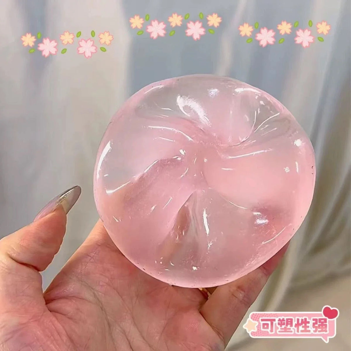 A hand holds a translucent pink squishy stress relief fidget toy with floral decorations against a light background.