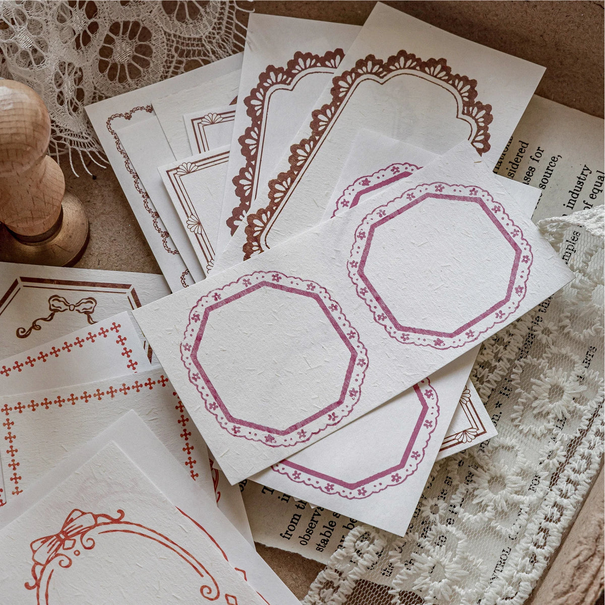A stack of vintage scrapbook paper sheets featuring delicate pink and maroon floral borders for journaling and crafts.