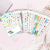 A collection of planner stickers in various colors and designs laid out on a pink surface.