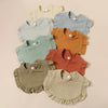 A set of eight cotton ruffle baby bibs in various muted earth tones including beige, sage green, mustard yellow, and terracot