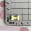 A small, pale yellow resin bone charm is placed on a ruler marked in centimeters.