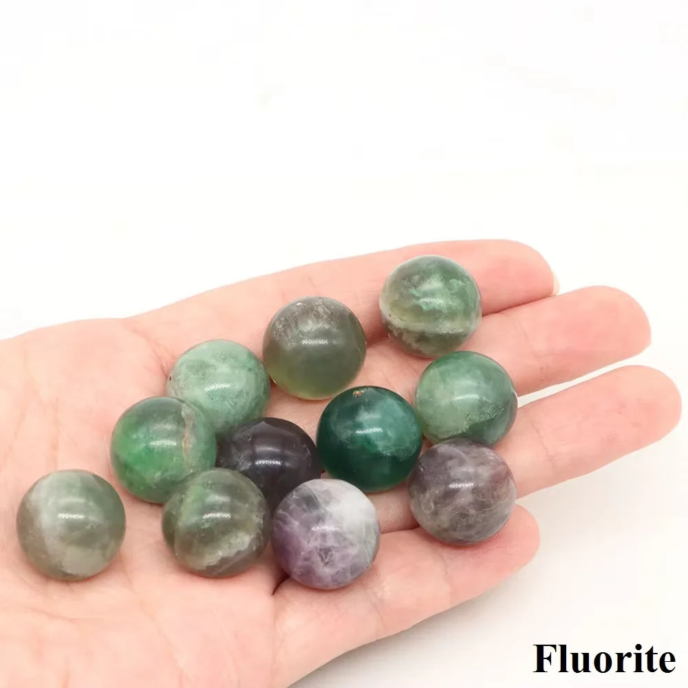 A hand holds several polished crystal spheres of natural amethyst and rose quartz.