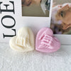 Two heart-shaped silicone molds for candles or soaps, one white and one pink, displayed in front of a framed photo.