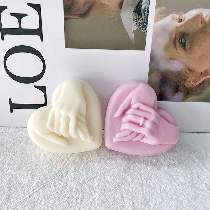 Two heart-shaped silicone molds for candles or soaps, one white and one pink, displayed in front of a framed photo.