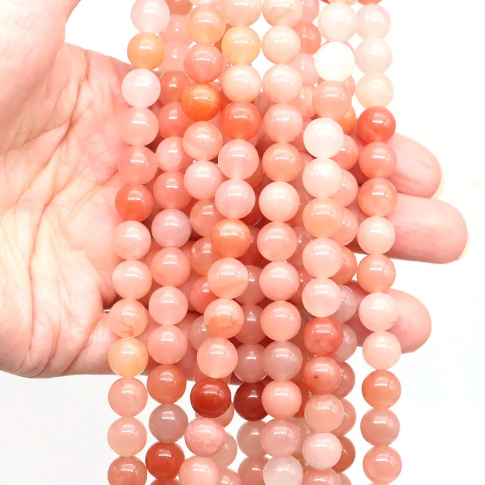 A hand holds a strand of round rose quartz beads in various shades of pink and orange.