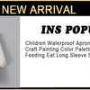 A light blue waterproof long-sleeve smock and dining bib for children, featuring a painted palette design.