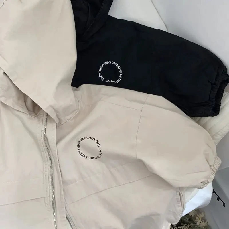 A beige hooded zip-up jacket with a black letter print on the chest, shown in a close-up view.