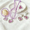 A set of five purple and silver princess jewelry accessories including a necklace and earrings displayed on a white cloth.