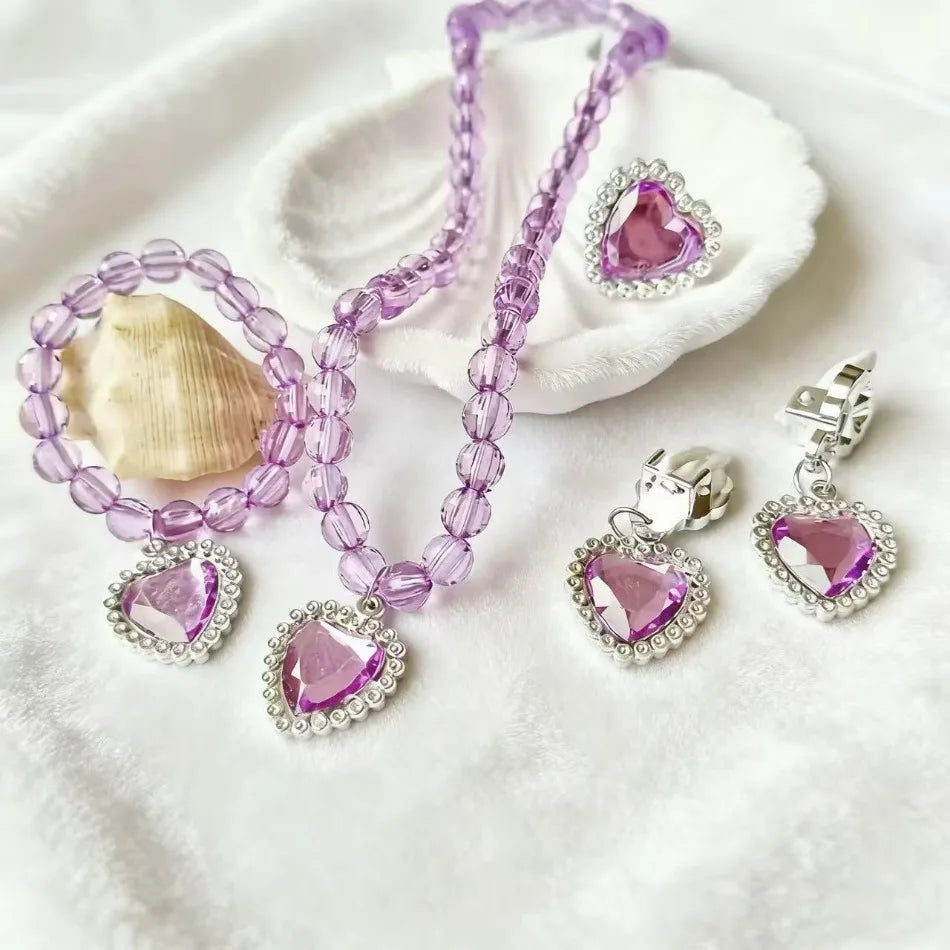 A set of five purple and silver princess jewelry accessories including a necklace and earrings displayed on a white cloth.