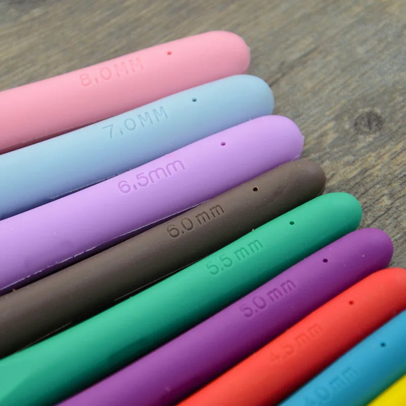 A close-up view of a set of ergonomic crochet hooks with various sizes and colors stacked diagonally on a wooden surface.