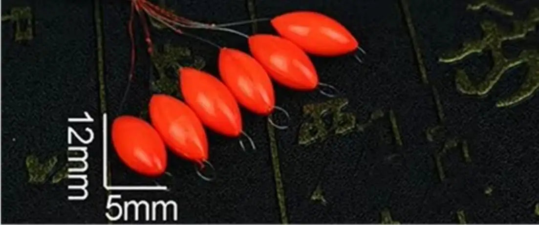 A row of bright orange oval fishing floats with attached bobber beads is displayed on a dark surface.