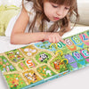 A young girl is looking at a Montessori busy book featuring colorful animal and number puzzles.