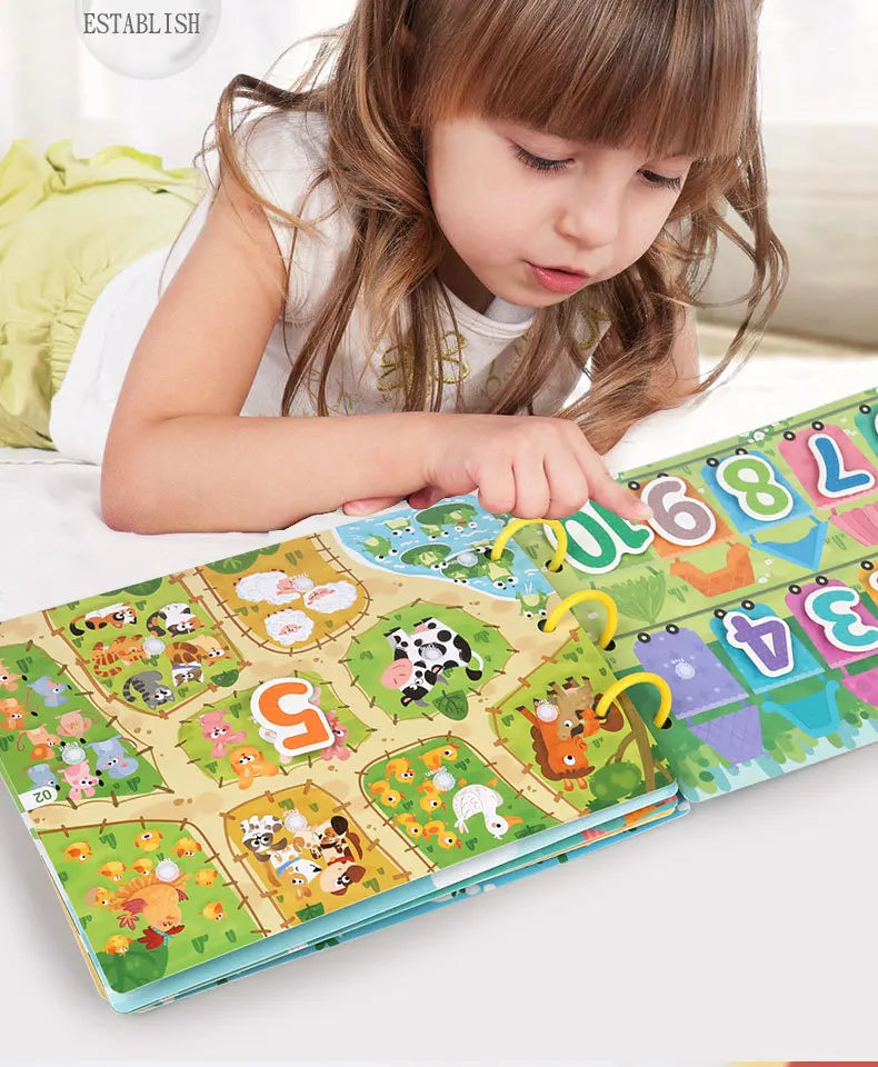 A young girl is looking at a Montessori busy book featuring colorful animal and number puzzles.