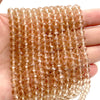 A hand holds a string of amber-colored Austrian faceted crystal beads for jewelry making.