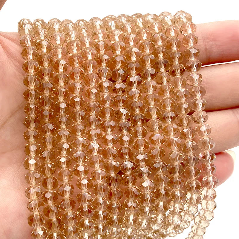 A hand holds a string of amber-colored Austrian faceted crystal beads for jewelry making.