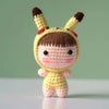 A handmade crochet doll kit featuring a yellow body, brown hair, and ears with red accents.