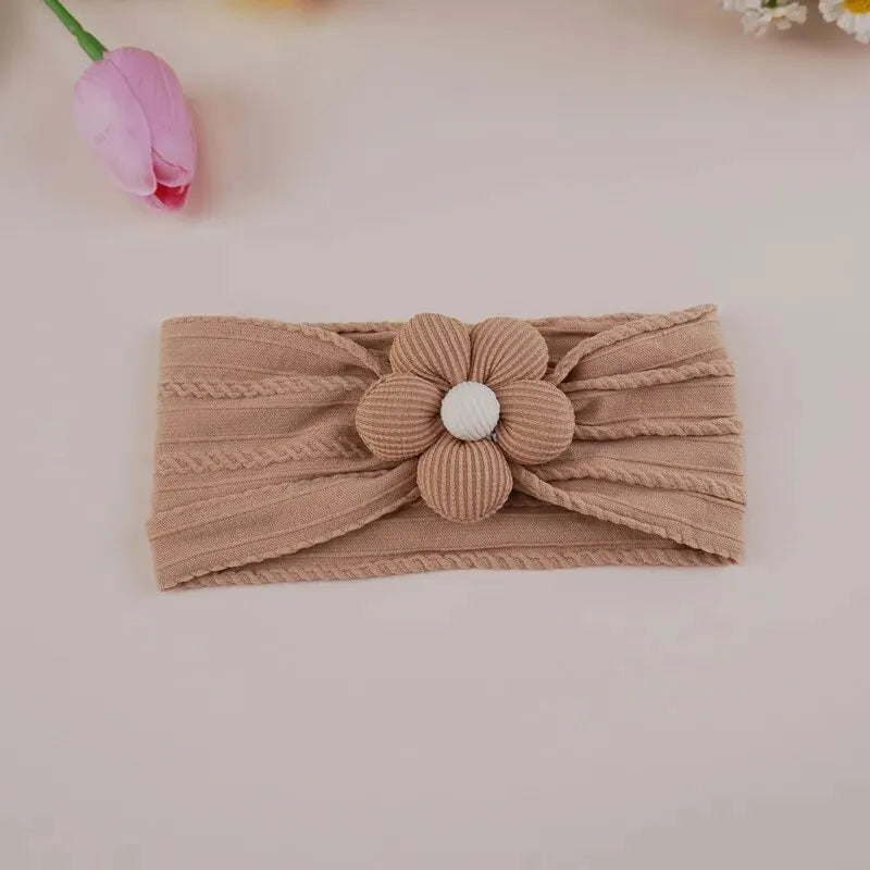 A beige floral elastic baby headband with a white center flower, displayed on a light background.