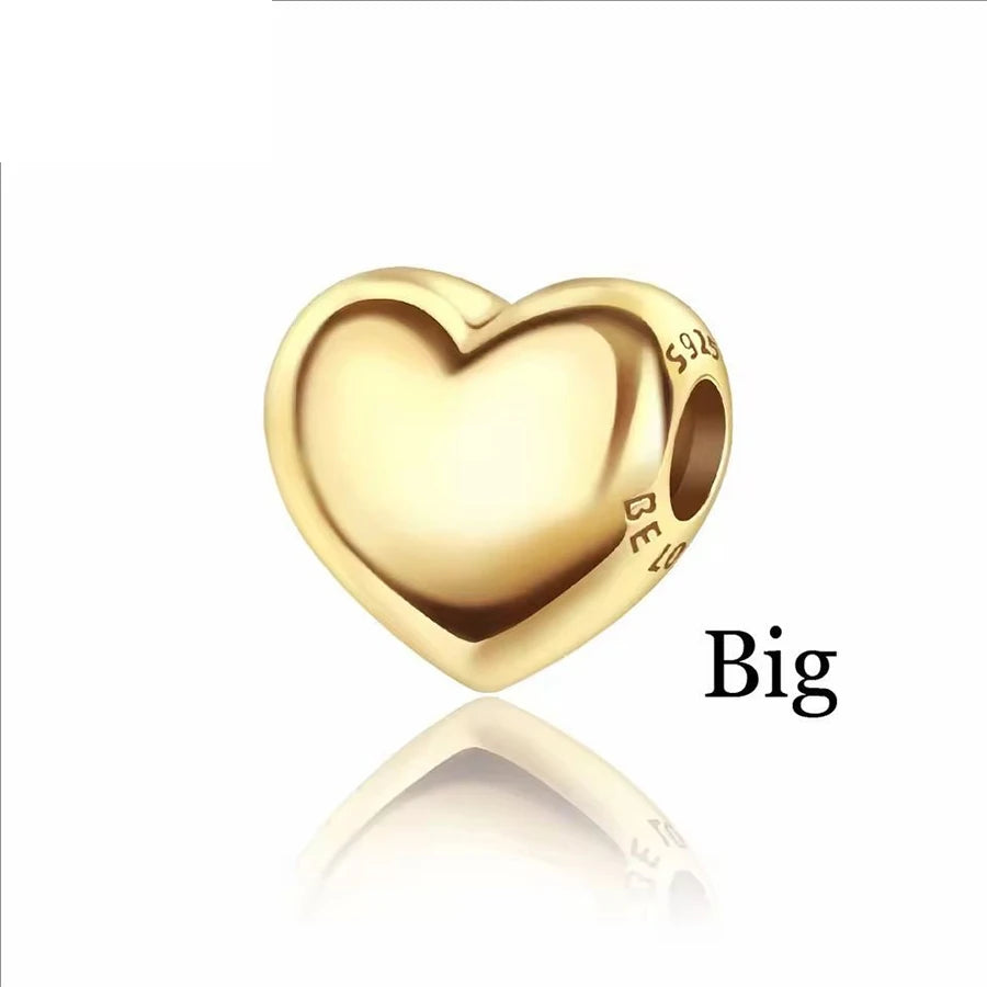 A large, smooth, gold-colored heart-shaped charm is shown on a reflective surface.