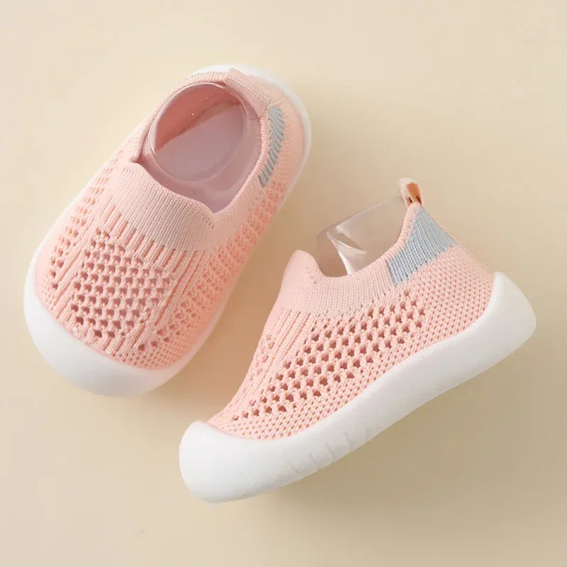 A pair of light pink breathable mesh slip-on sneakers for toddlers with white soles and gray accents.