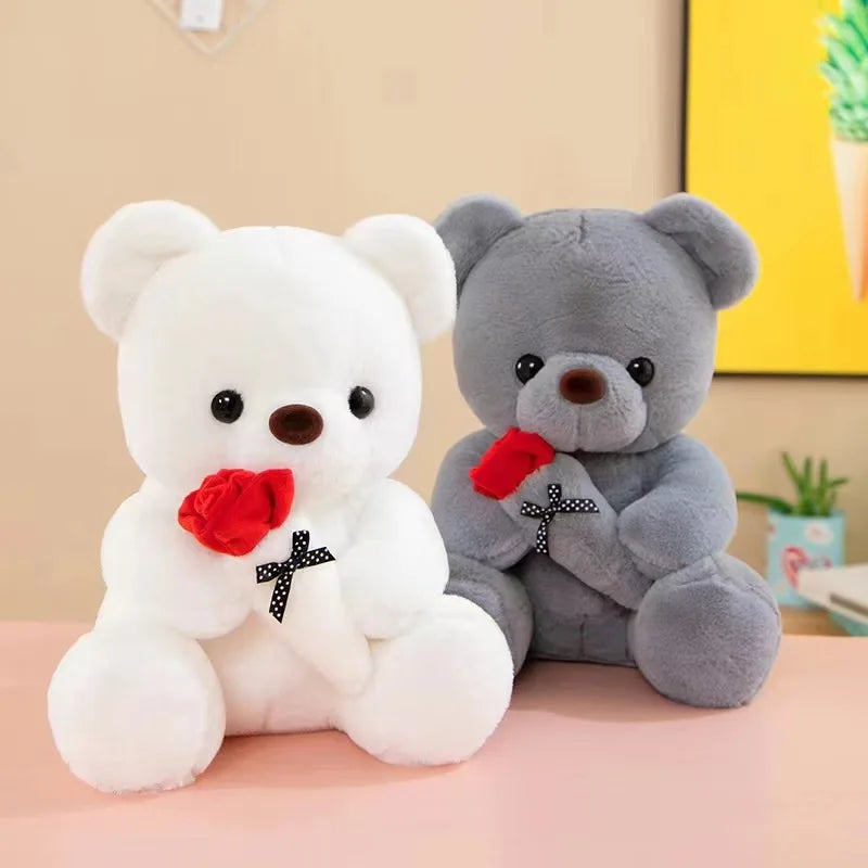 A white teddy bear and a gray teddy bear are shown holding red roses on a pink surface.