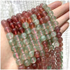 A hand holds a string of round, polished natural stone beads in shades of pink, red, and green.