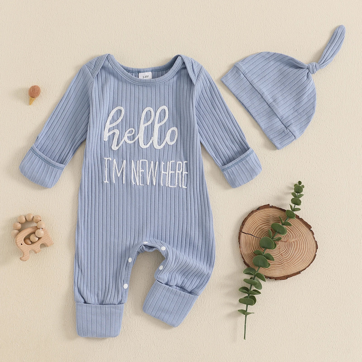 A light blue baby boy long sleeve ribbed romper and matching hat lying on a beige surface.