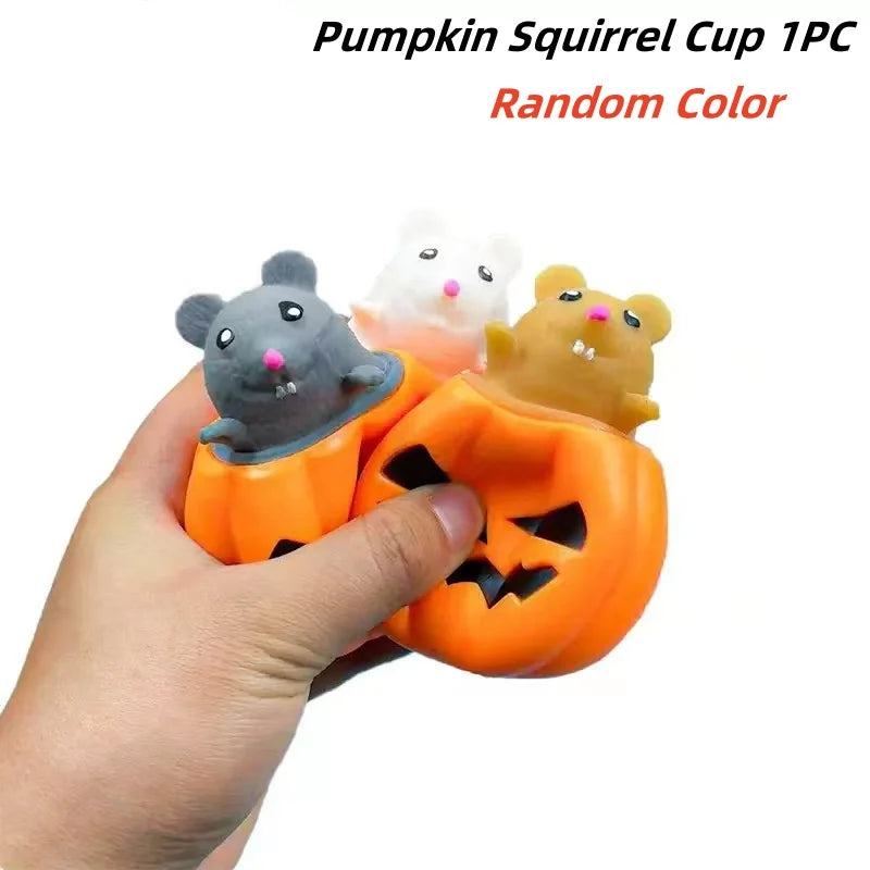 A hand holds an orange pumpkin squeeze stress ball and two small, random-colored squirrel cups.