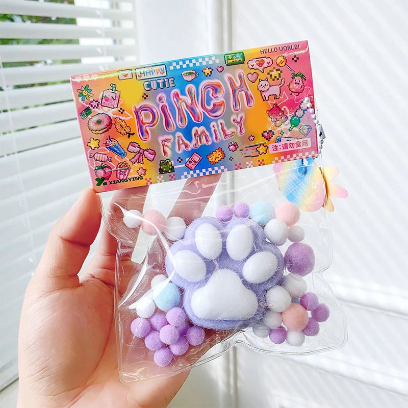 A clear plastic pouch containing a purple and white cat paw squishy stress relief toy and a colorful packaging card.