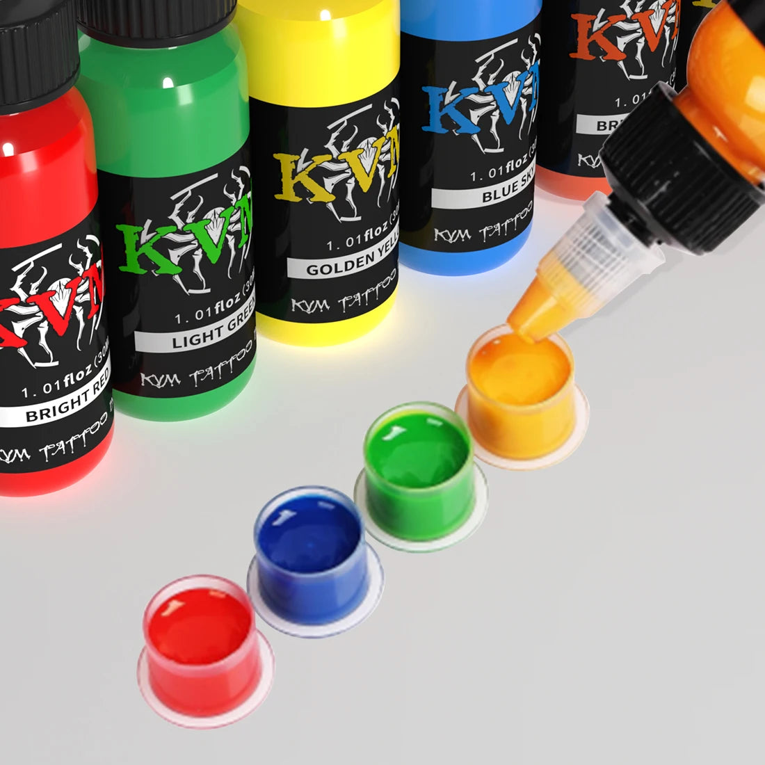 A collection of 14 colored tattoo inks in glass bottles and a dropper, showing various shades like bright red, green, yellow,