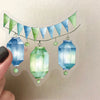 A string of green and blue triangular pennant banners hangs above three glass-shaped lanterns.