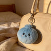 A light beige handbag with a blue squishy dumpling keychain plush attached to the zipper pull.