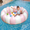 A young girl is sitting inside a pink and white inflatable round toddler pool in blue water.