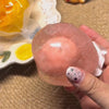 A hand holds a pink, translucent stress ball with a star design against a beige background.