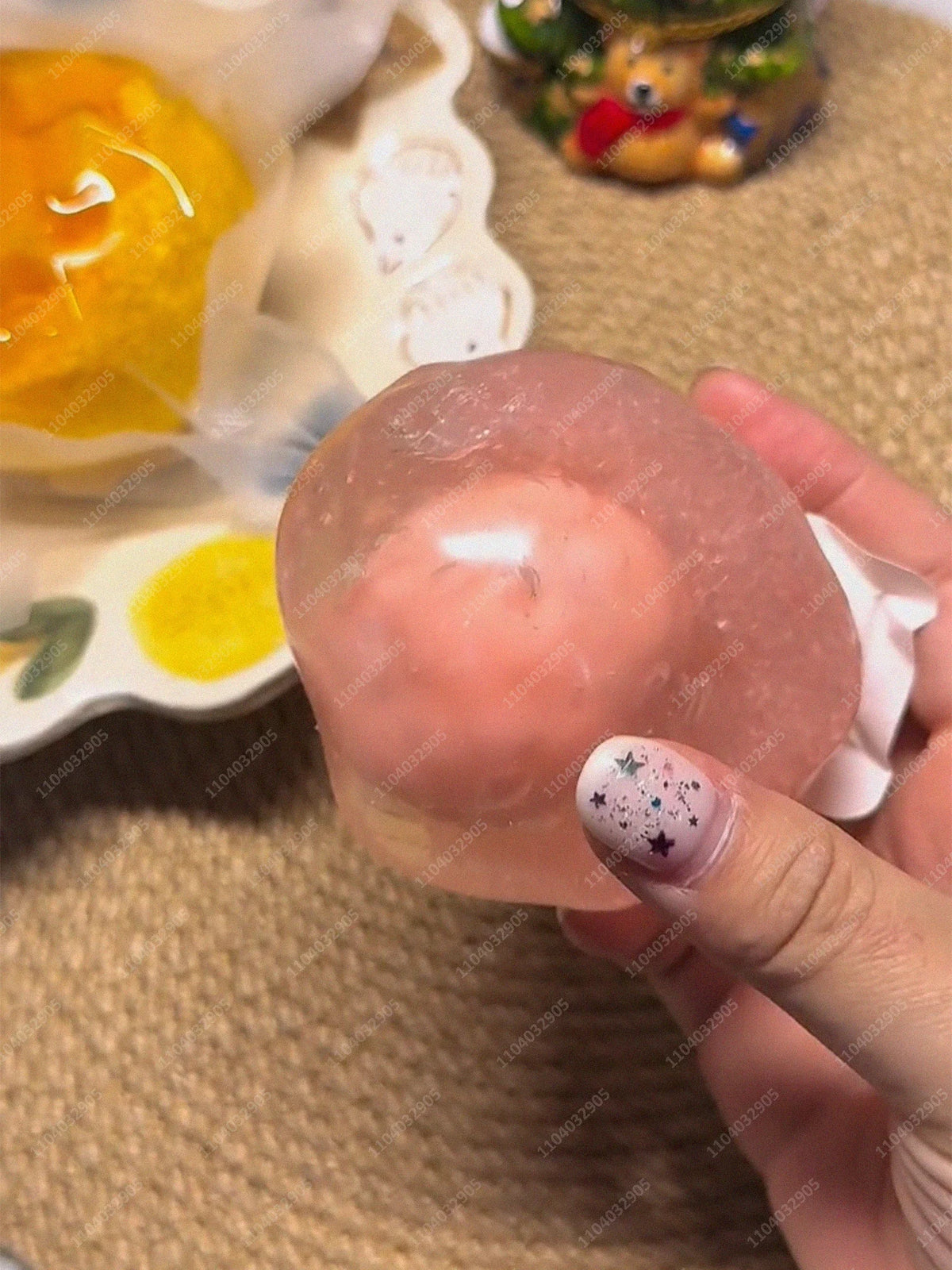 A hand holds a pink, translucent stress ball with a star design against a beige background.