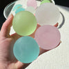 A hand holds several round, translucent squishy stress cubes in pastel shades of green, pink, and blue.