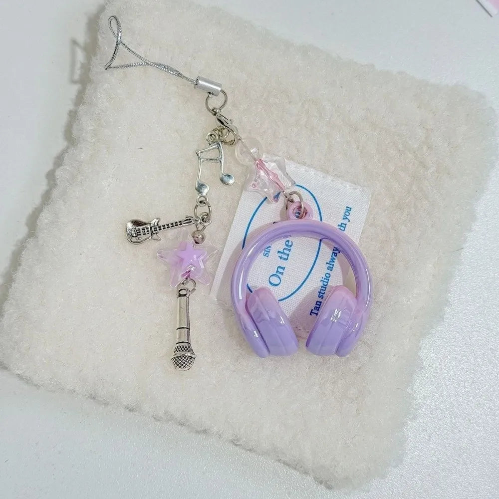 A beaded wing cross phone lanyard keychain with a purple earbud resting on a white fluffy surface.