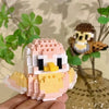 A hand holds a colorful parrot micro building blocks set featuring pink, yellow, and white pieces.