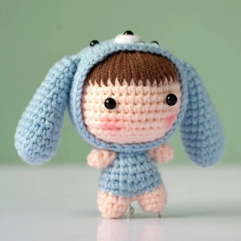 A handmade light blue crochet doll wearing a hood with brown hair and black eyes.