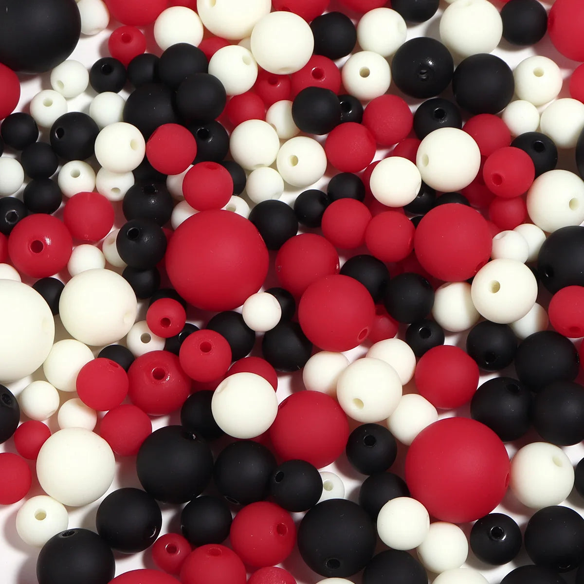 A close-up view of various matte acrylic beads in black, white, and red colors scattered on a white surface.